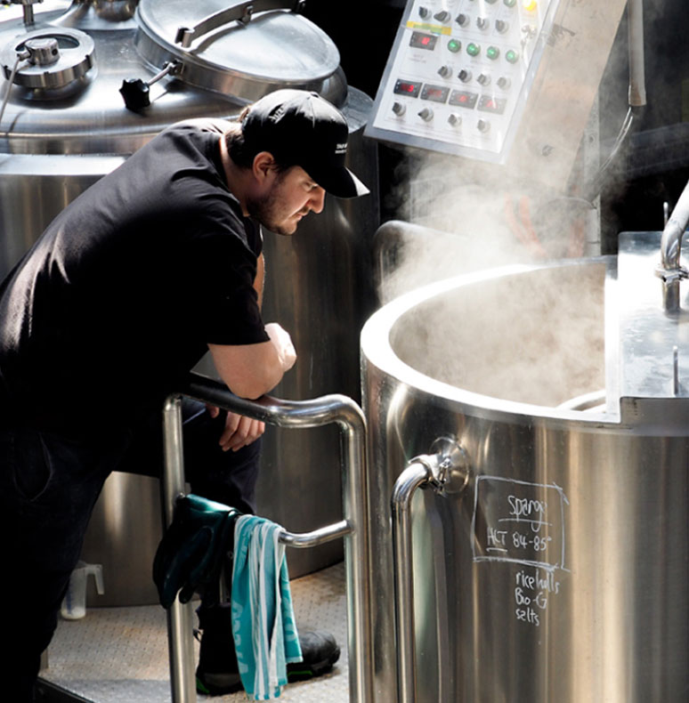 Brewer checking on beer in vat at Tar Barrel Brewery and Distillery